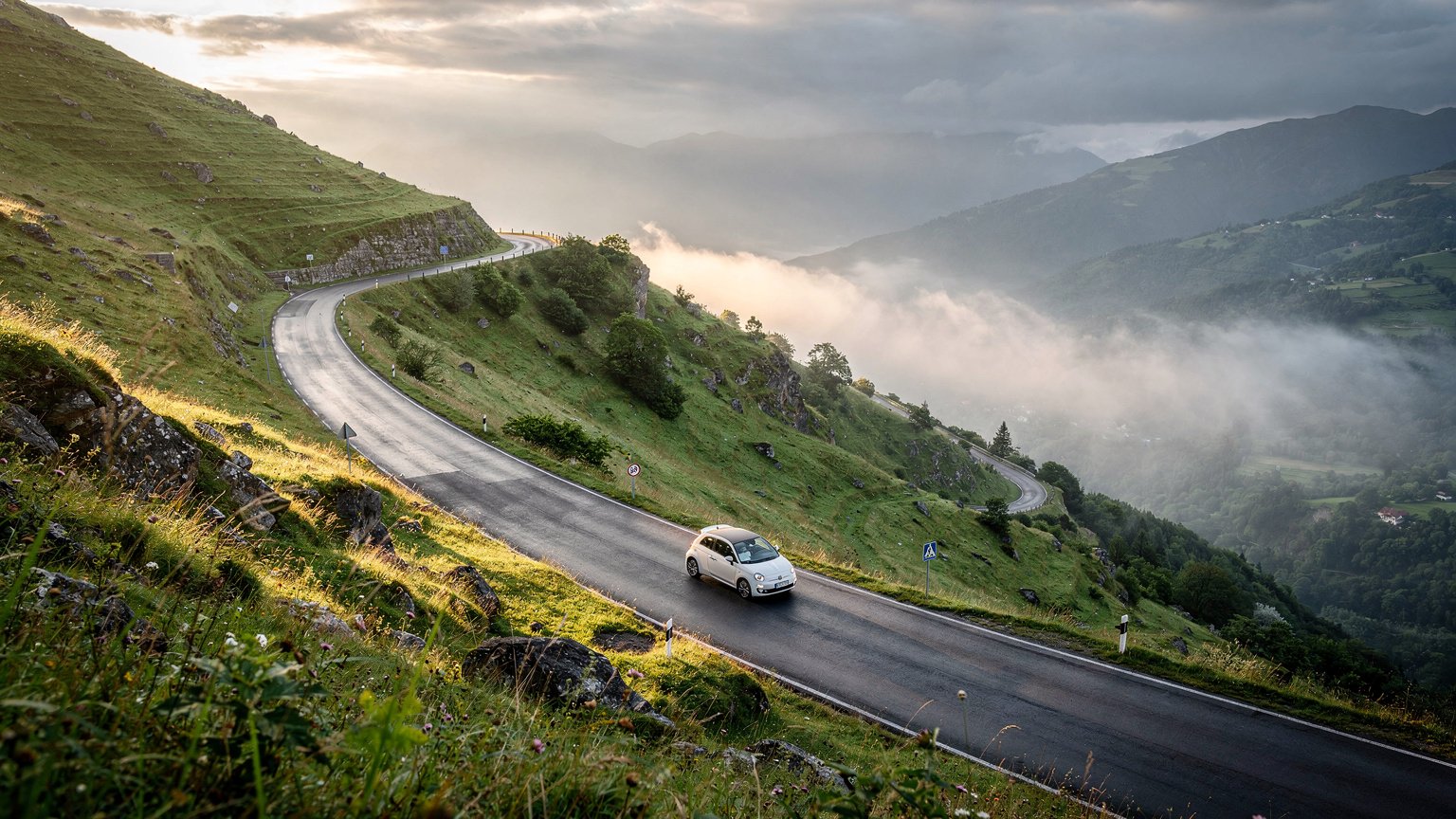 Green valley with a switchback road and a small white car (illustrative image)