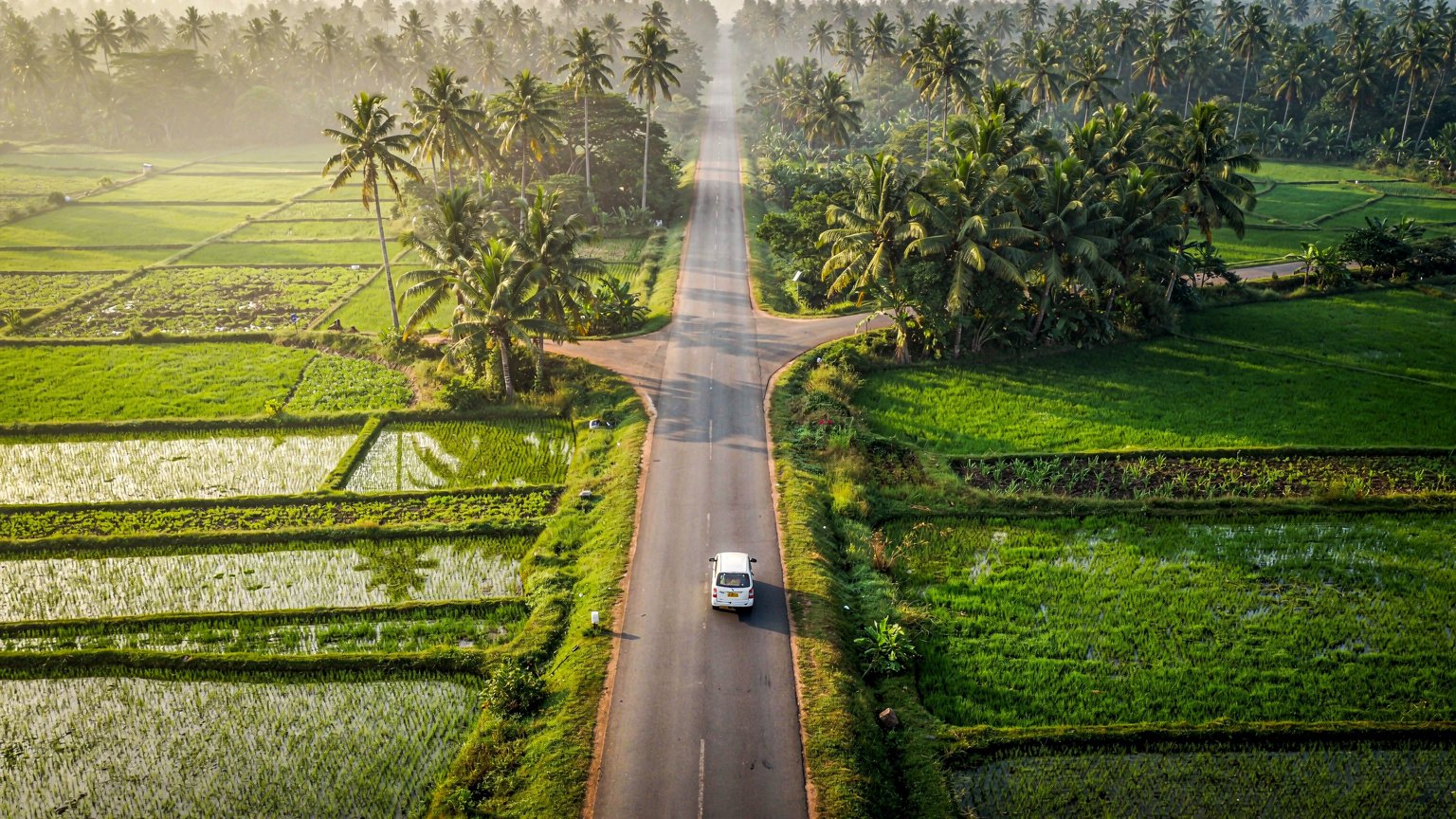 Aerial view of a road fork through green farmland with a white taxi (illustrative image)
