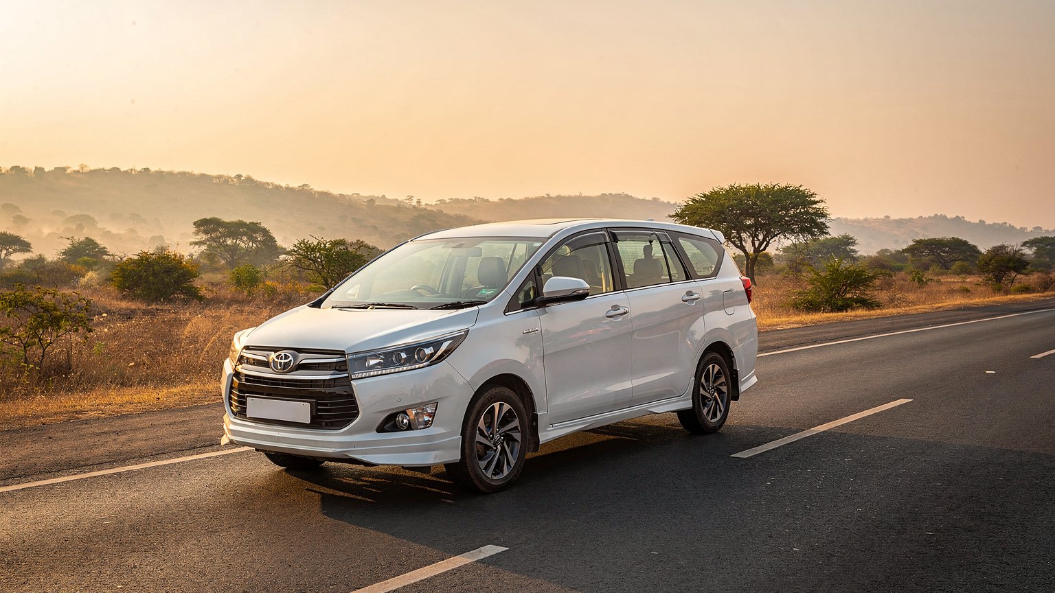 White MPV taxi on a multi-lane highway at sunrise (illustrative image)