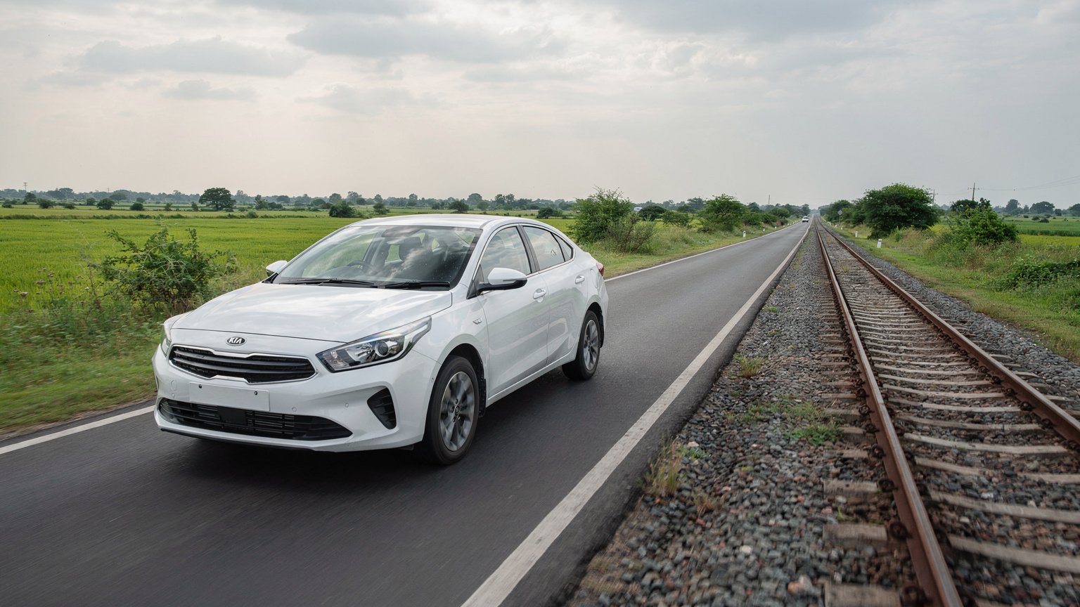 White sedan on a road beside a railway line (illustrative image)