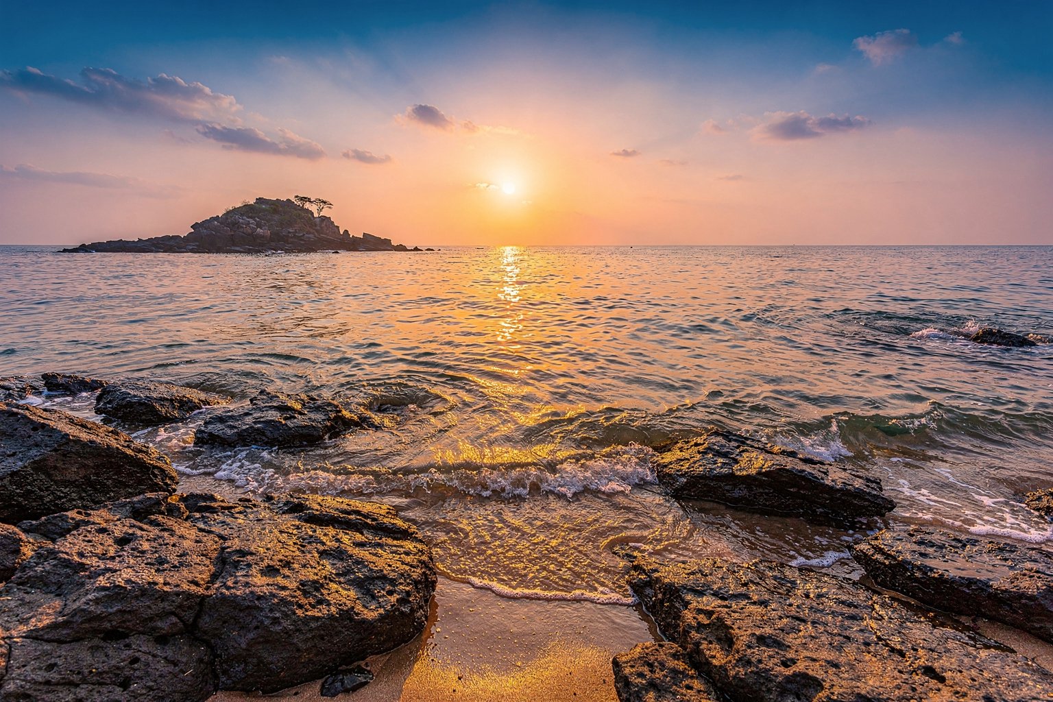 Sunrise over the sea with rocks and a distant islet in southern India (illustrative image)