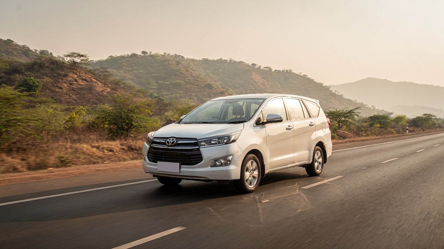 White MPV taxi on a highway beside hills (illustrative image)