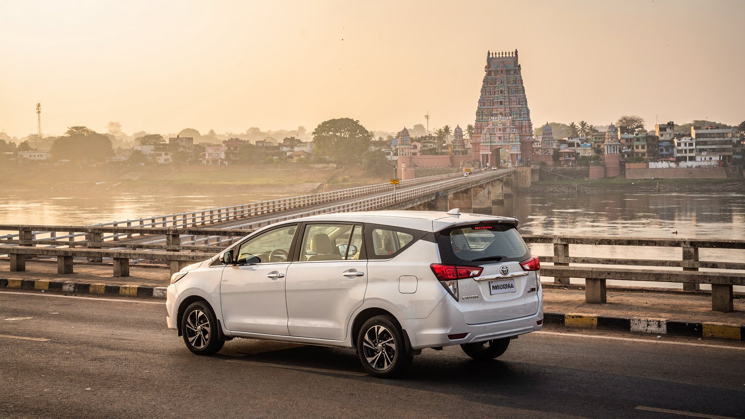 White MPV taxi on a river bridge with a temple tower in the distance (illustrative image)