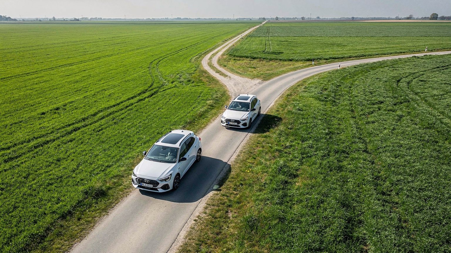 Two roads diverging across green fields with white cars (illustrative image)